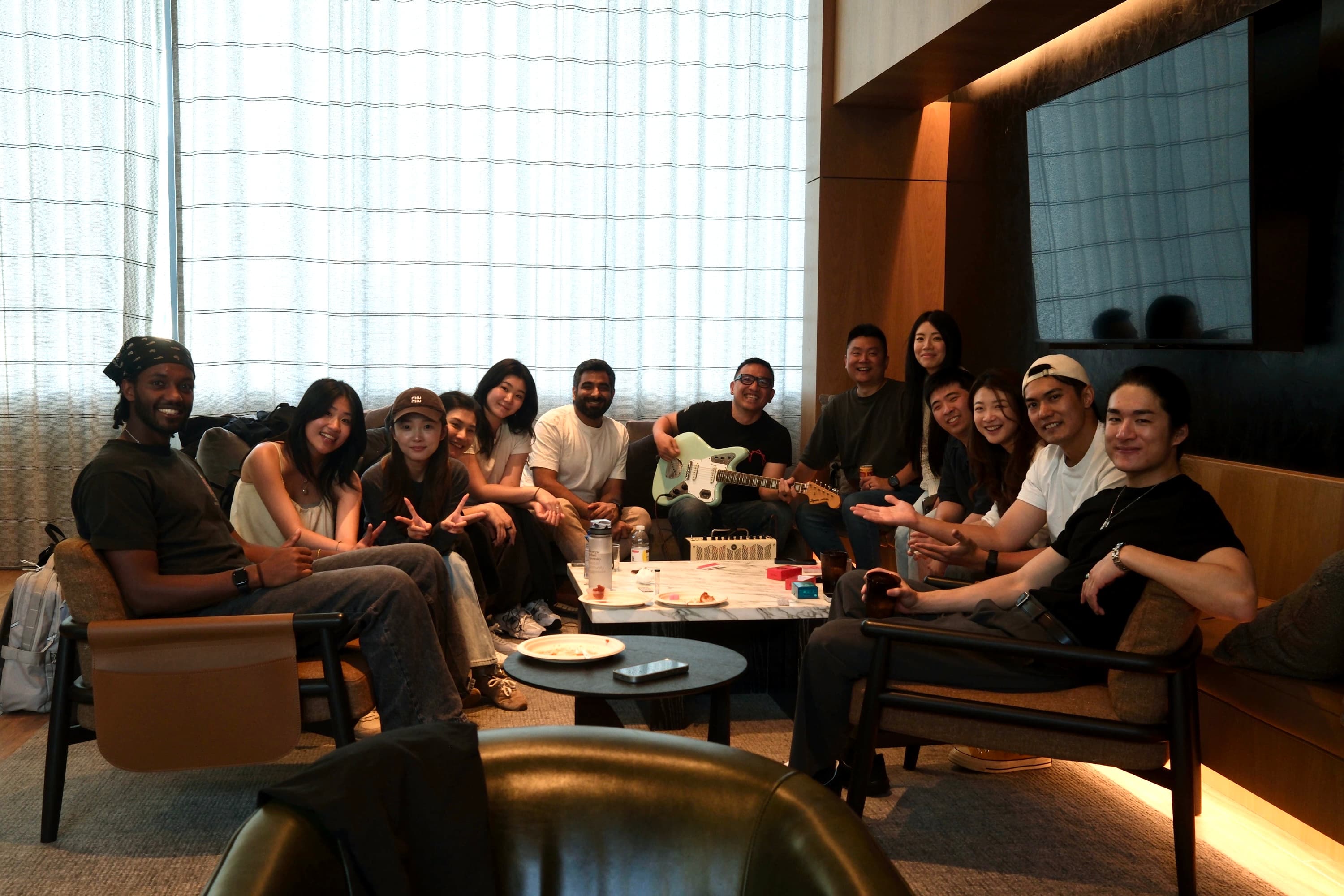 A large group posing together in a lounge, one person playing guitar.
